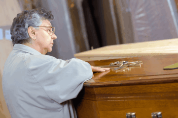 Woman tenderly touching coffin in funeral home.